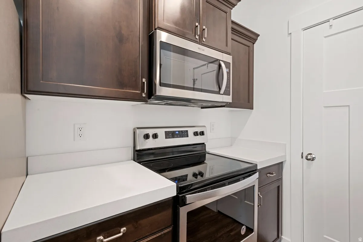 Kitchen area featuring dark wood-finish cabinetry, stainless steel appliances, solid surface countertops, and a white interior door with panel detailing