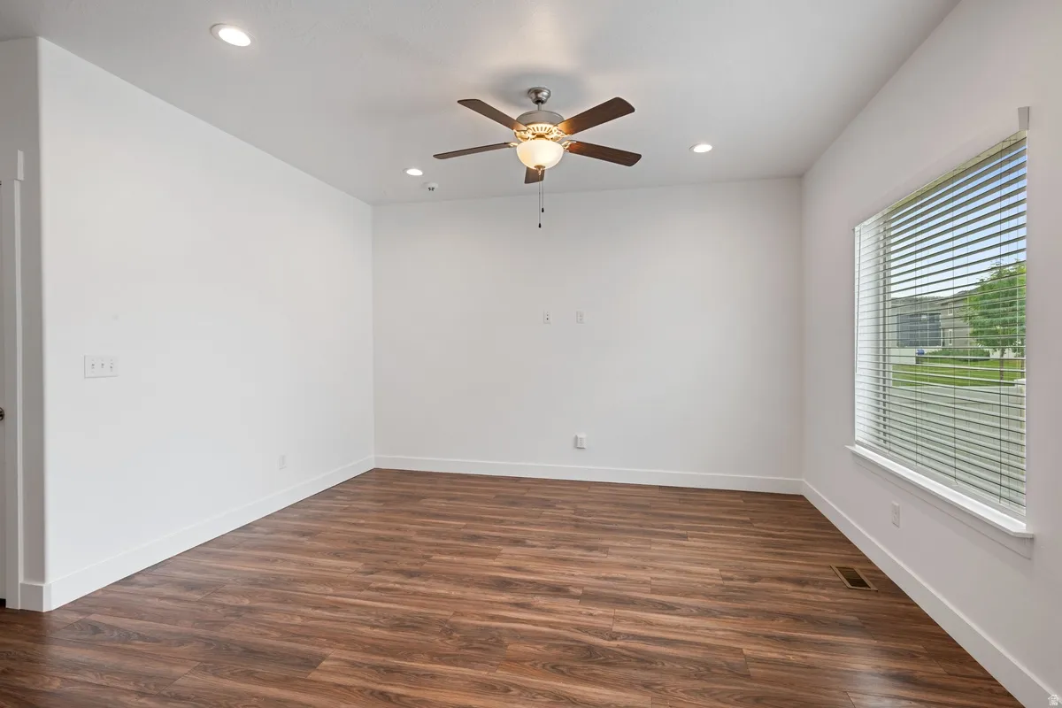 Spacious room featuring wood-finish flooring, white baseboards, and a ceiling fan with integrated lighting