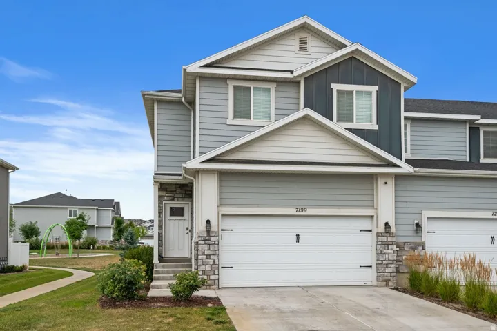 Modern townhouse exterior featuring light blue siding with dark blue accents, a white garage door, and stone facade detailing