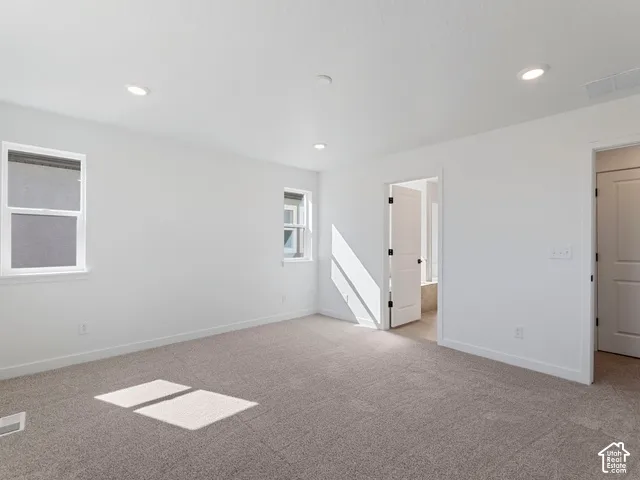 Neutral tone carpeting, recessed lighting, white walls, and bright white window trim