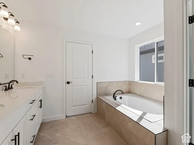 Spacious bathroom featuring a built-in bathtub, a double vanity with stone countertops, and tile flooring
