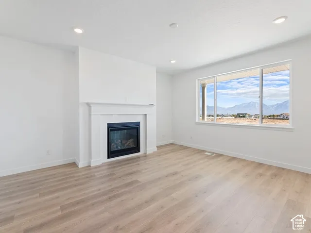 Recessed lighting, wood-finish flooring, white trim, a built-in fireplace with white mantel, and a large window