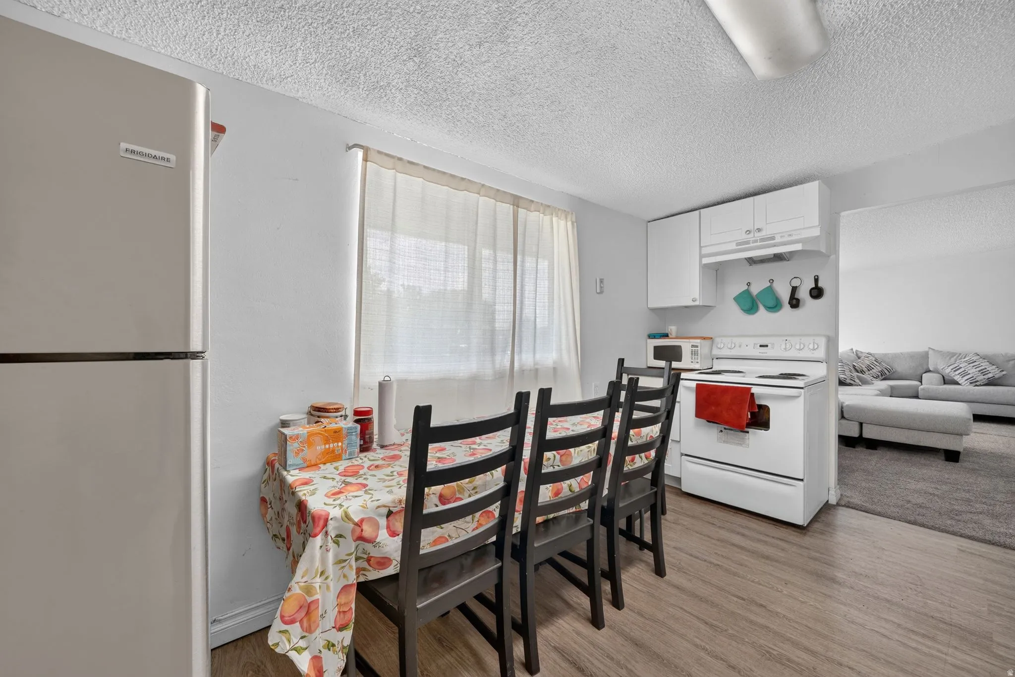 Kitchen area featuring wood-finish flooring, white cabinetry, and a white electric range with overhead microwave space