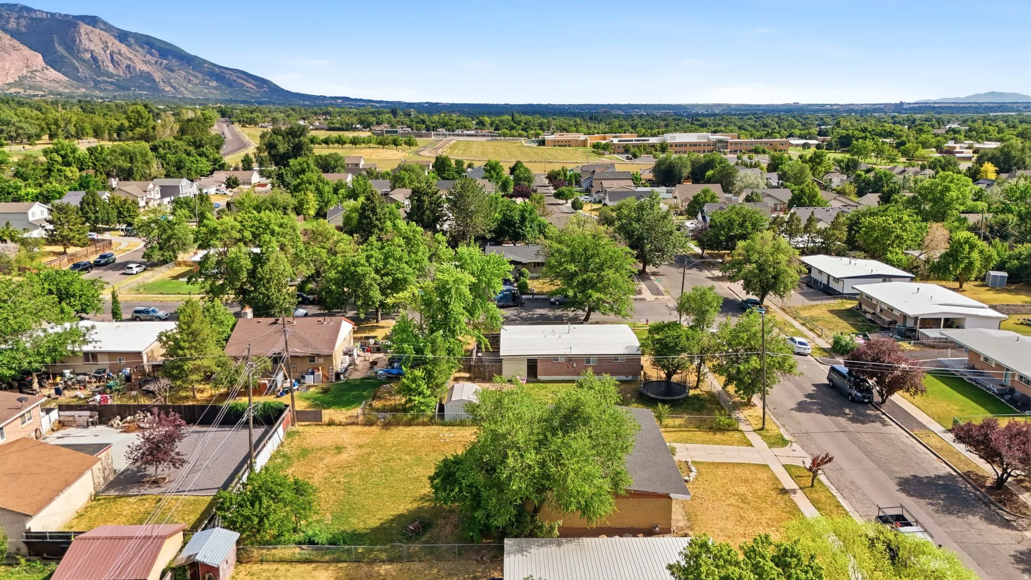 Aerial perspective showcasing a neighborhood with mature trees, green spaces, and mountain terrain in the distance