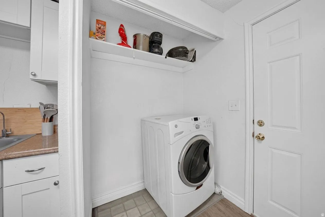 Dedicated laundry area featuring a front-loading washing machine, overhead shelving, and a paneled door with brass hardware