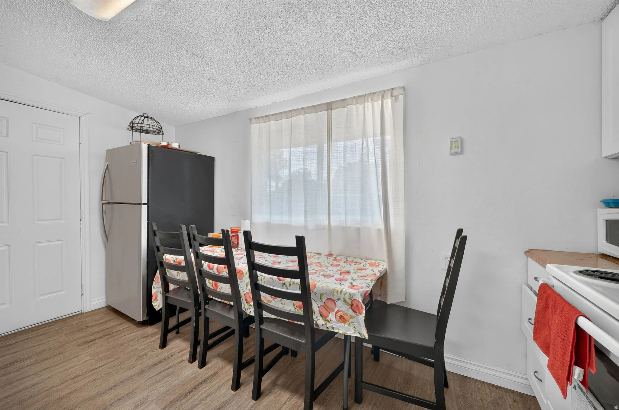 Bright dining area featuring wood-finish flooring, a white paneled door, and a window with sheer curtains