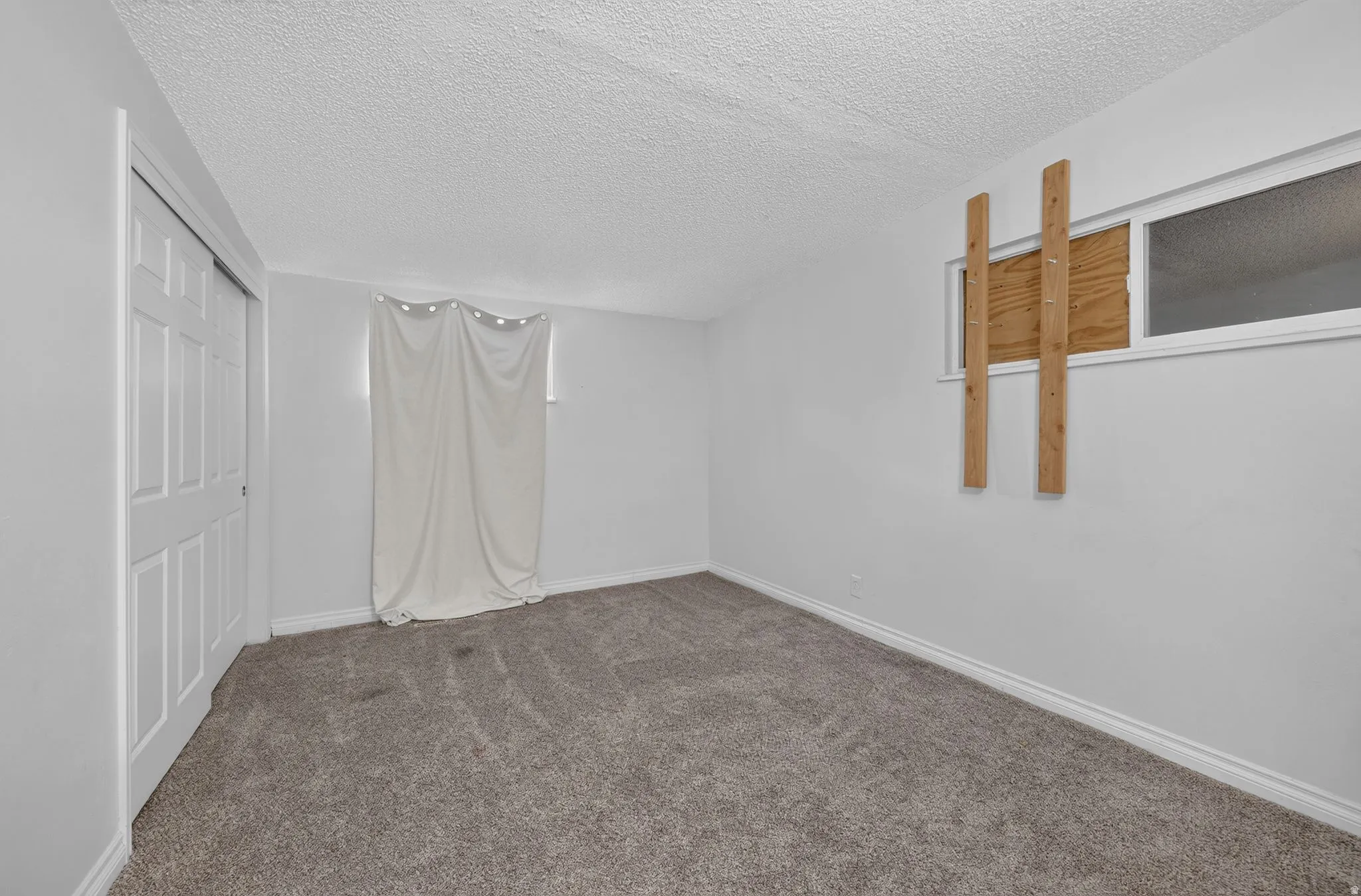 Carpeted room with white walls, baseboards, and textured ceilings