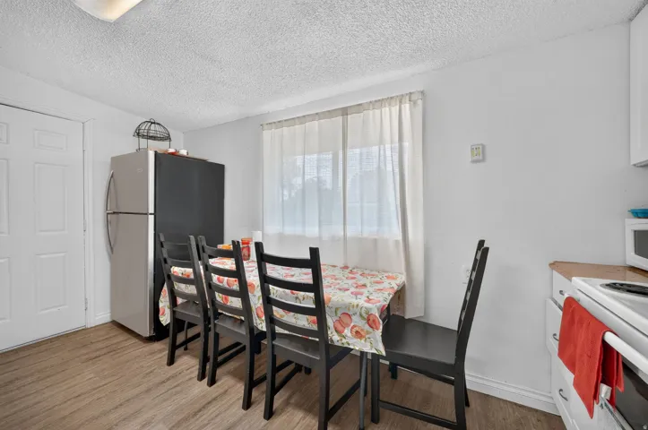 Bright dining area featuring wood-finish flooring, a white paneled door, and a window with sheer curtains