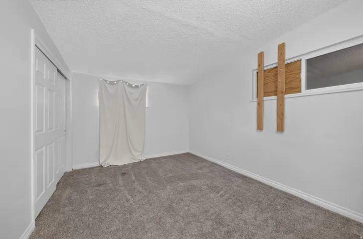 Carpeted room with white walls, baseboards, and textured ceilings