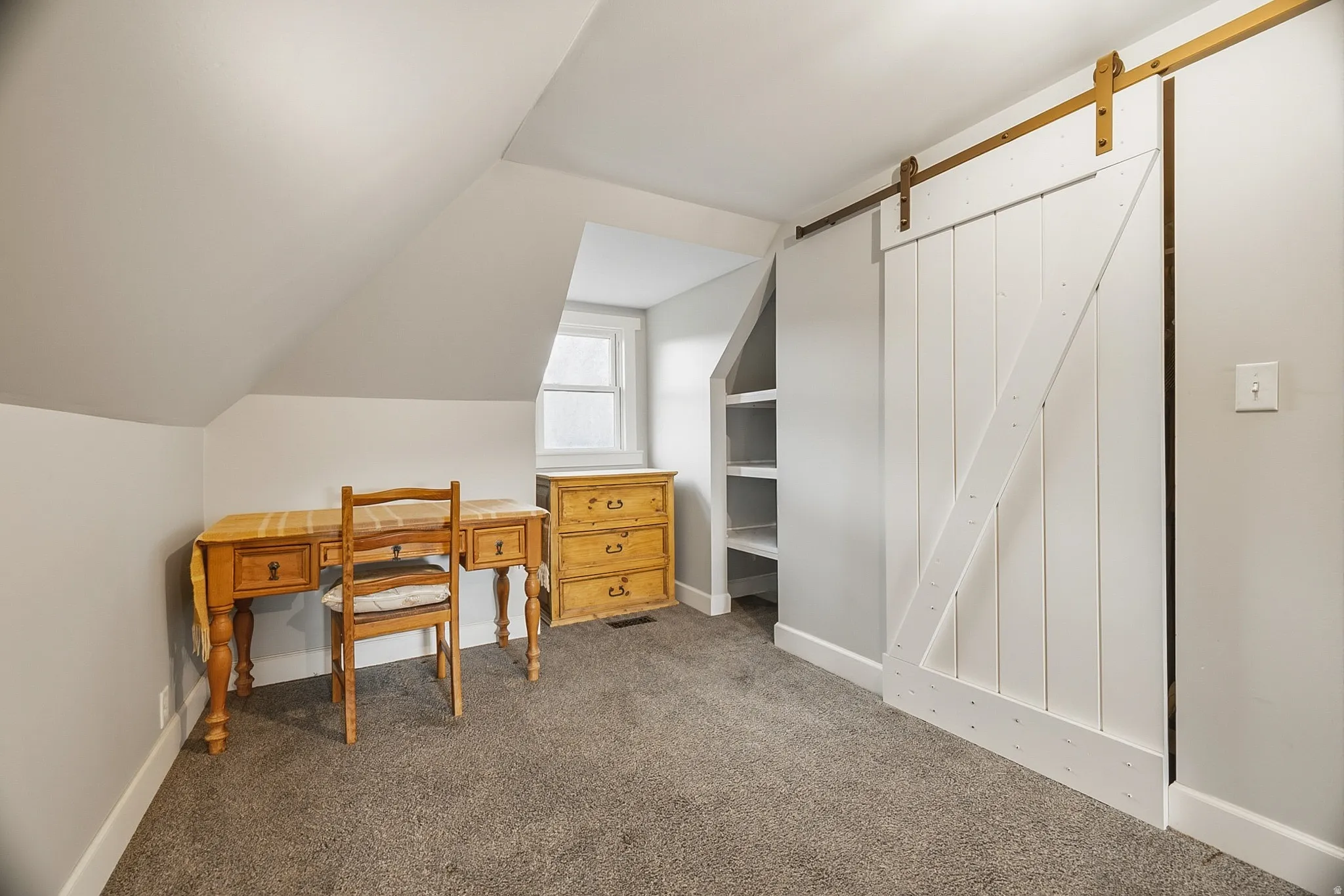 Attic space featuring a white barn door, built-in shelving, a window, and gray carpeting