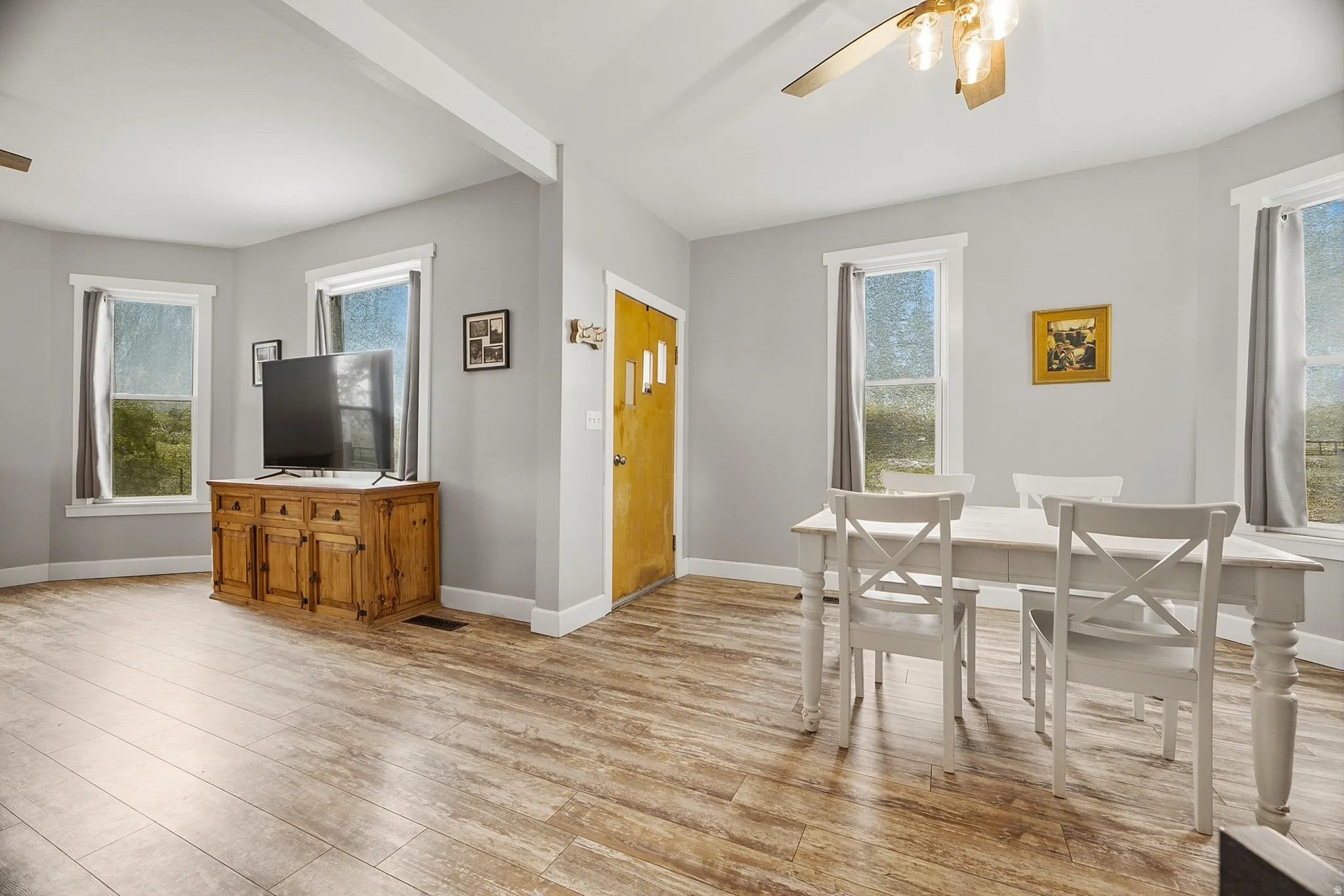 Spacious room with wood-finish flooring, light grey walls, and multiple windows
