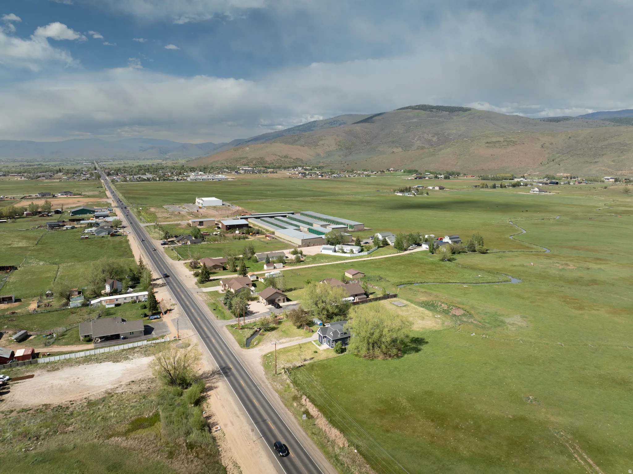 Expansive green fields featuring a long paved road with scattered residential properties