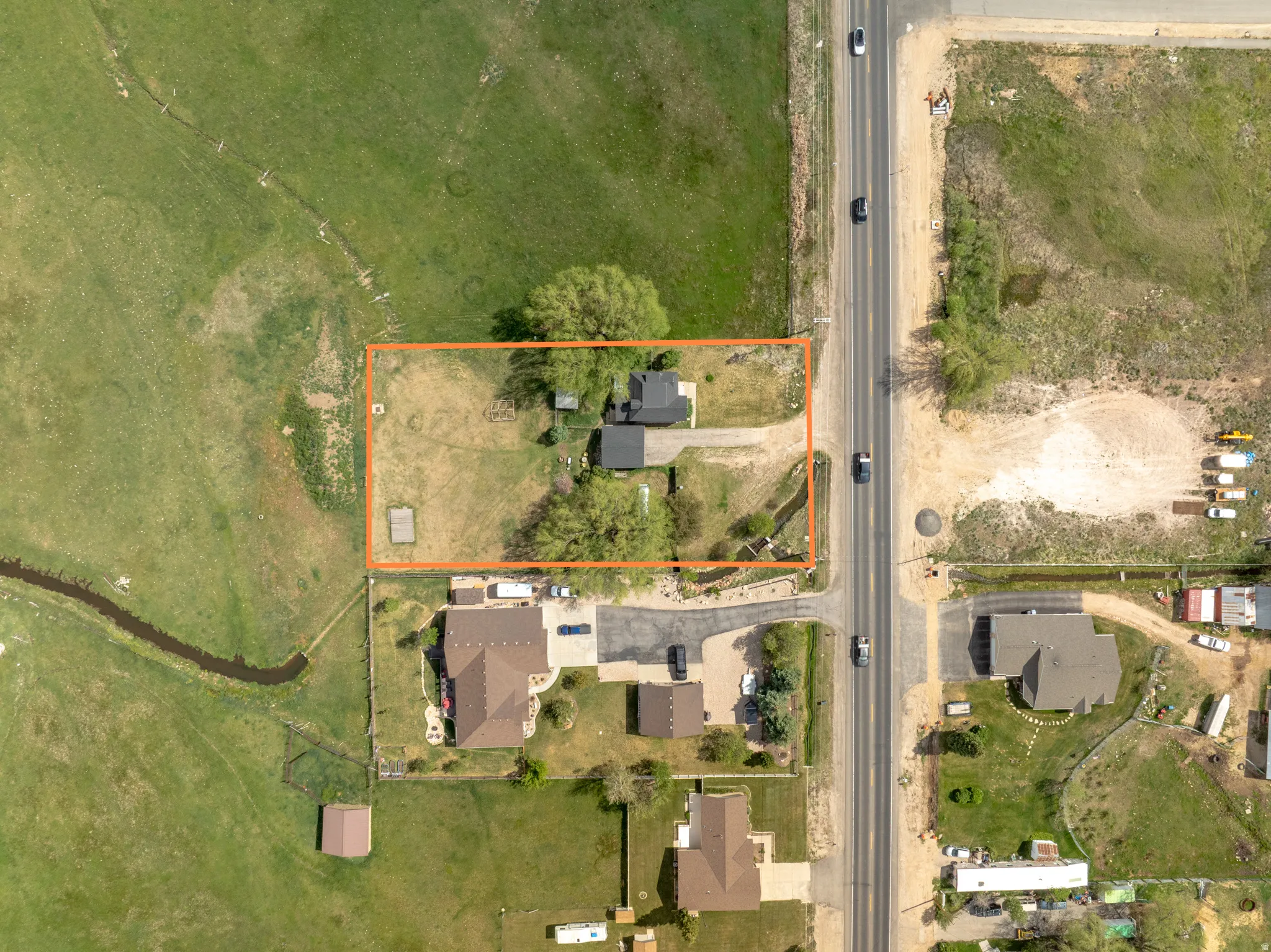 Aerial perspective showcasing a parcel of land with two structures, mature trees, and direct road frontage