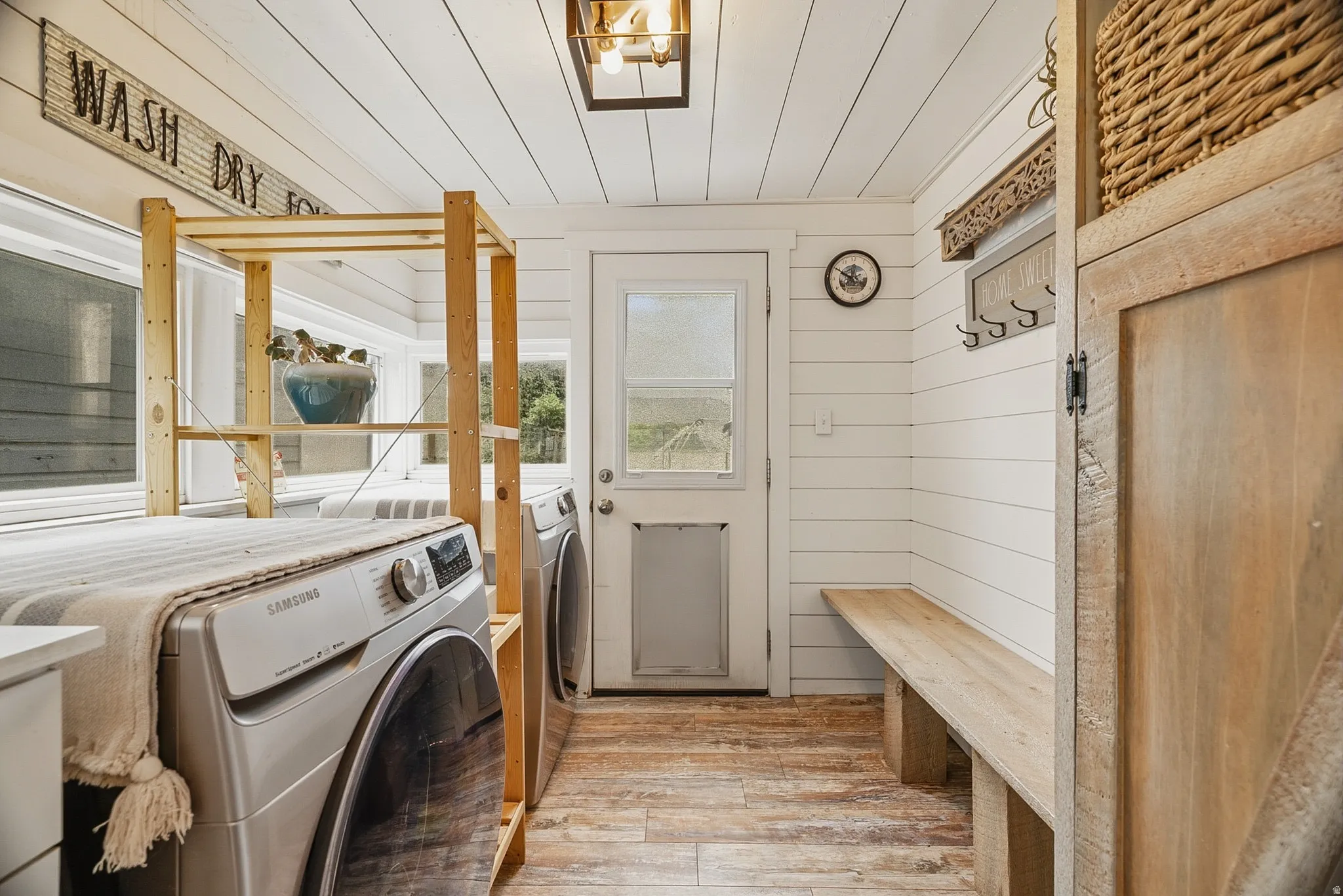 Laundry area featuring wood-finish flooring, shiplap walls, and a built-in wooden bench