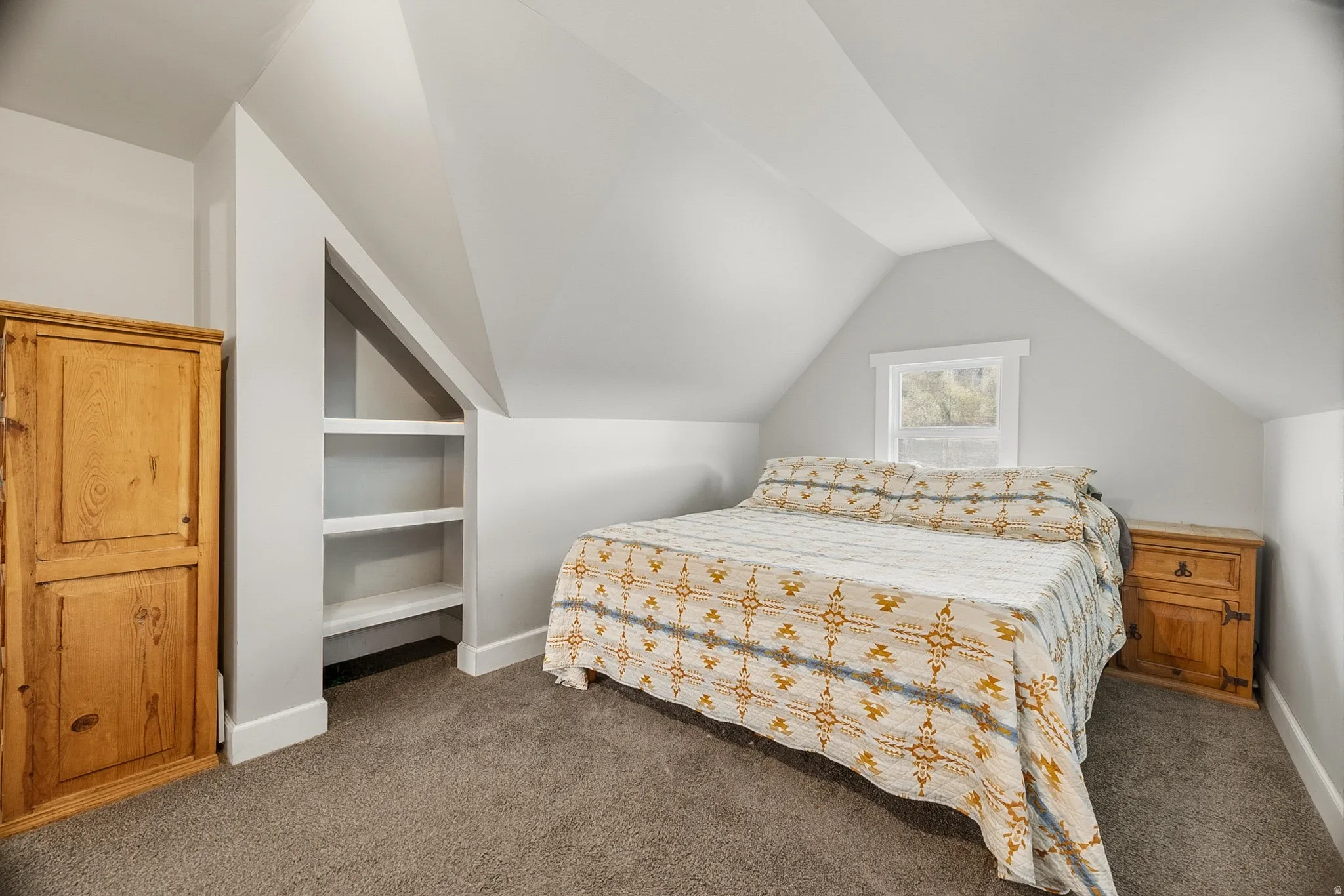 Carpeted room featuring a white-trimmed window, built-in shelving, vaulted ceilings, and light gray wall finishes