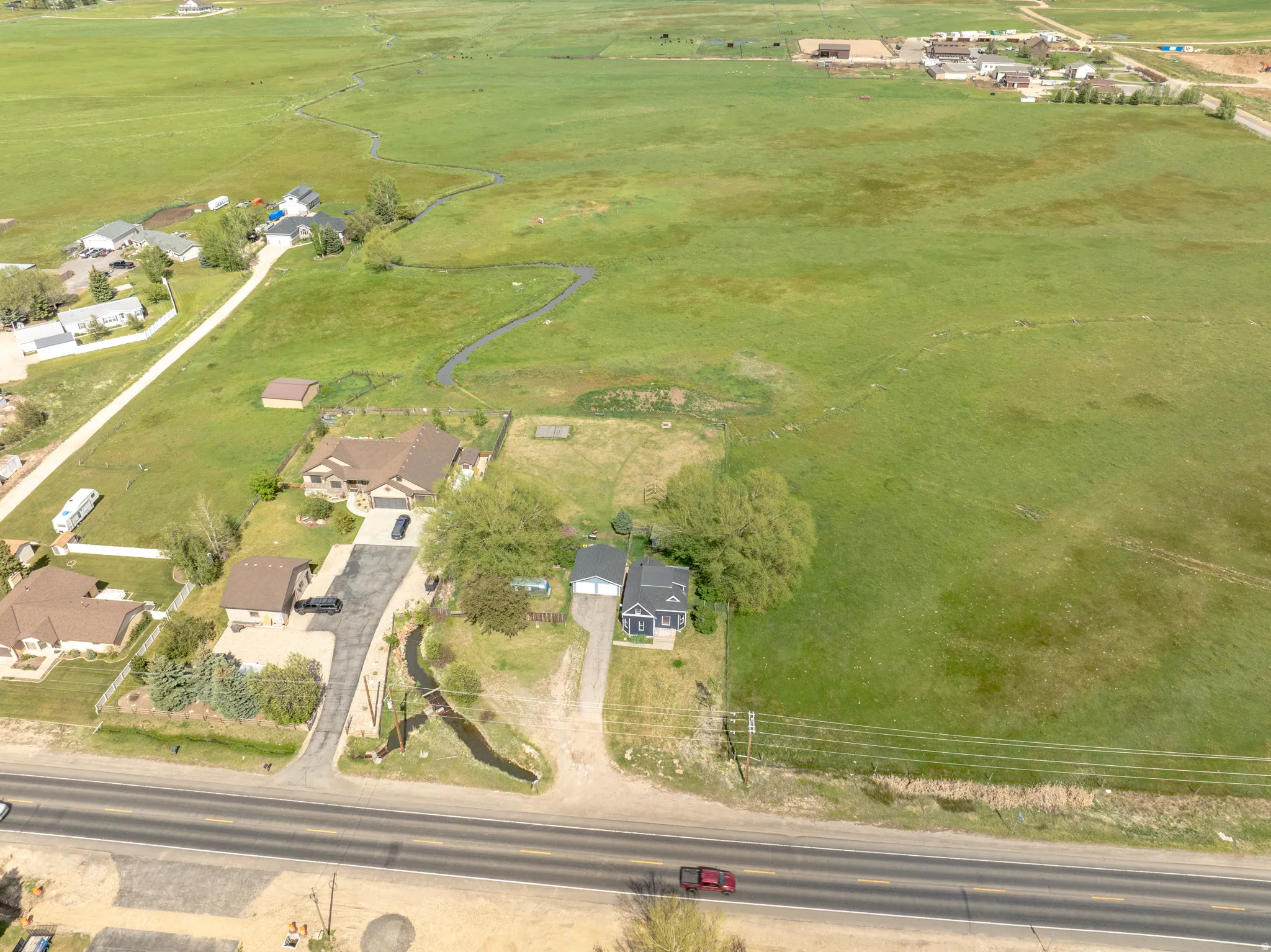 Expansive green acreage with a visible creek, offering a rural setting with residential properties
