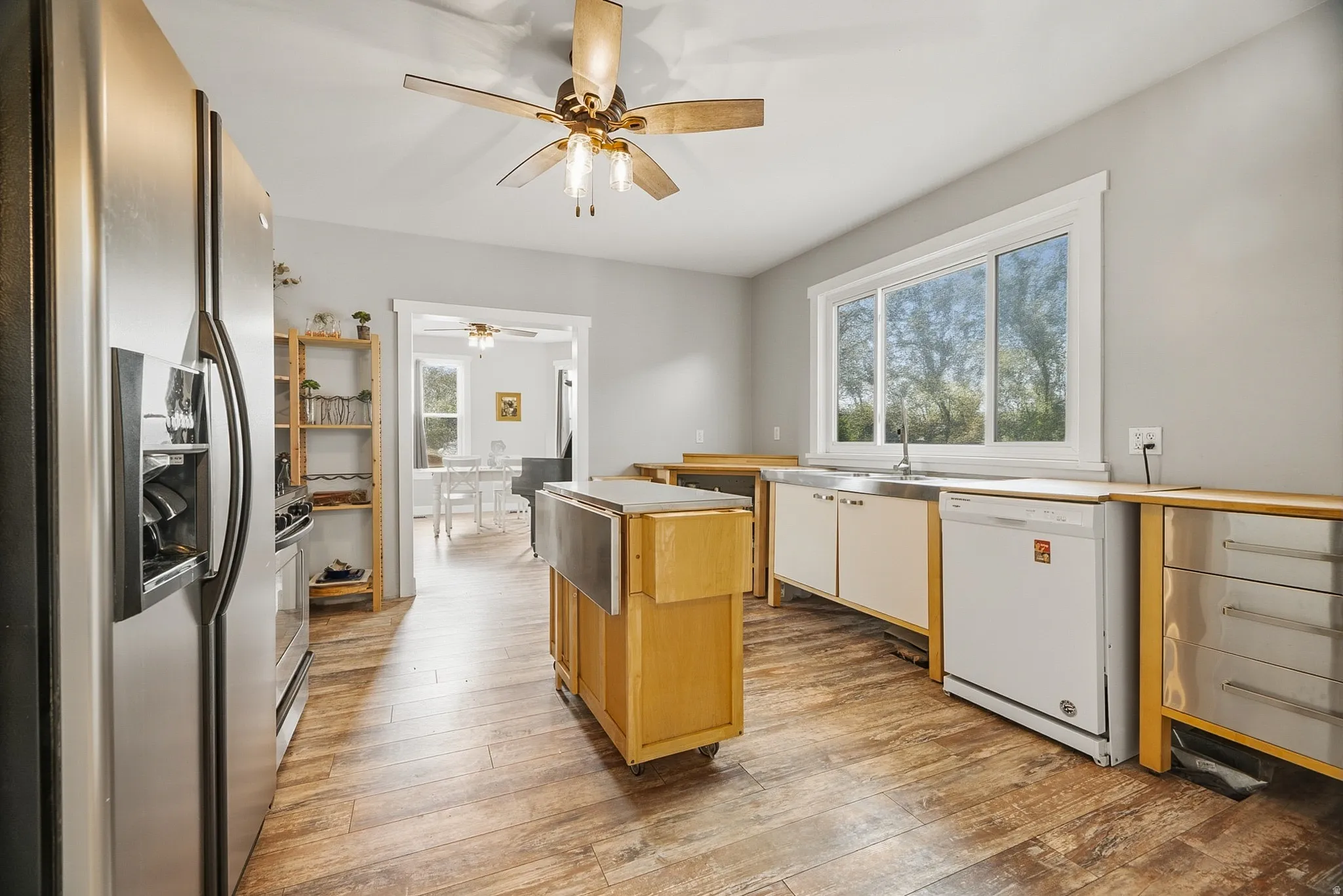 Open kitchen featuring wood-finish flooring, stainless steel refrigerator, white dishwasher, and a large window above the sink