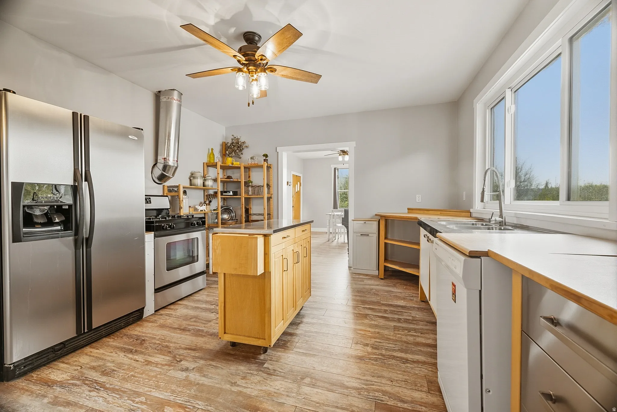 Kitchen featuring wood-finish flooring, stainless steel appliances, a center island with cabinetry, light-toned countertops, and multiple windows