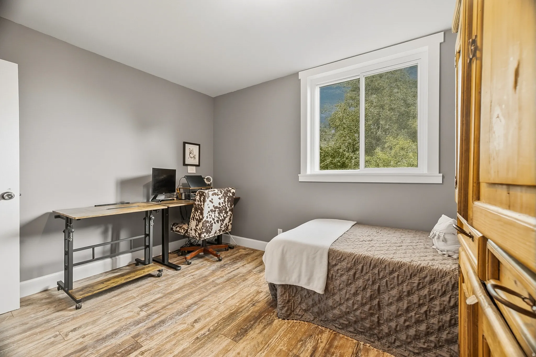 Bedroom featuring wood-finish flooring, a bright window with white trim, gray wall paint, and a built-in wooden wardrobe