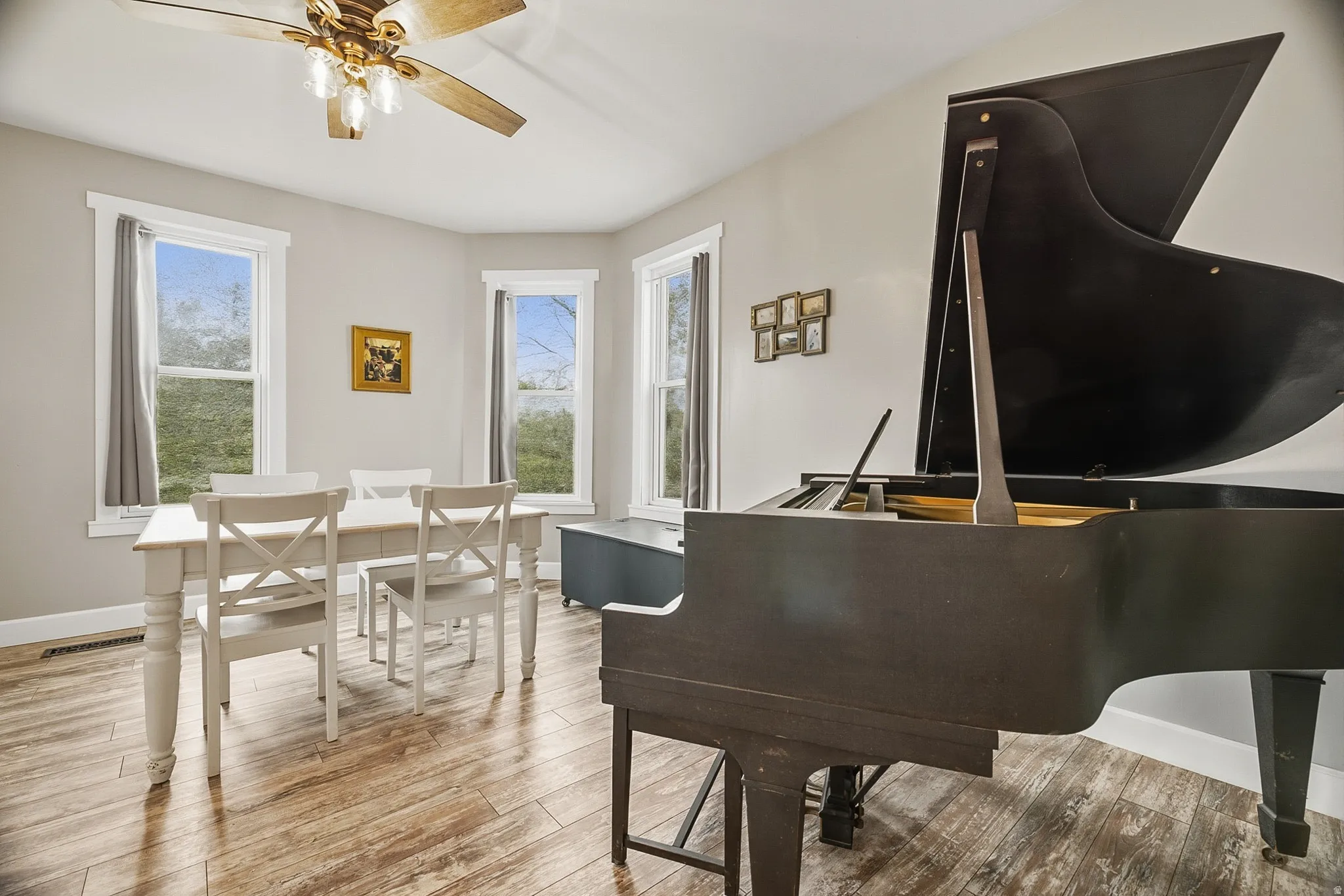 Spacious room featuring light wood-finish flooring, light gray walls, and multiple large windows with white trim