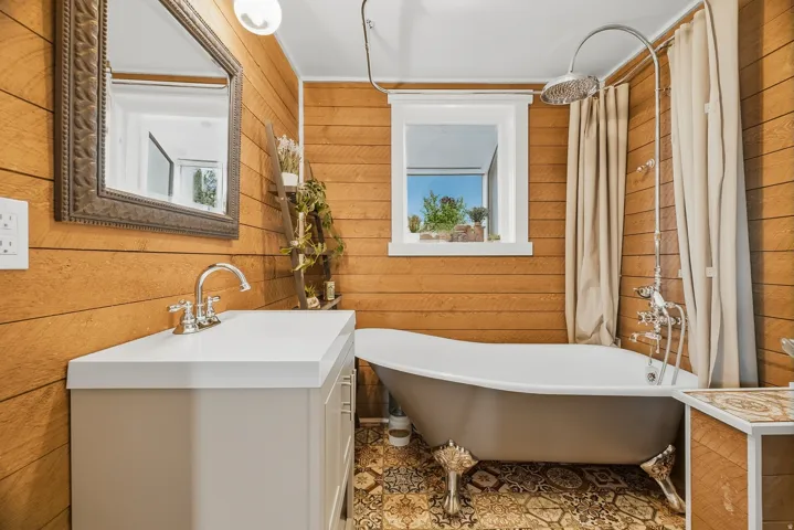 Bathroom featuring wood plank walls, a freestanding clawfoot bathtub with a rain showerhead, a single-sink vanity with a white countertop, and patterned floor tile