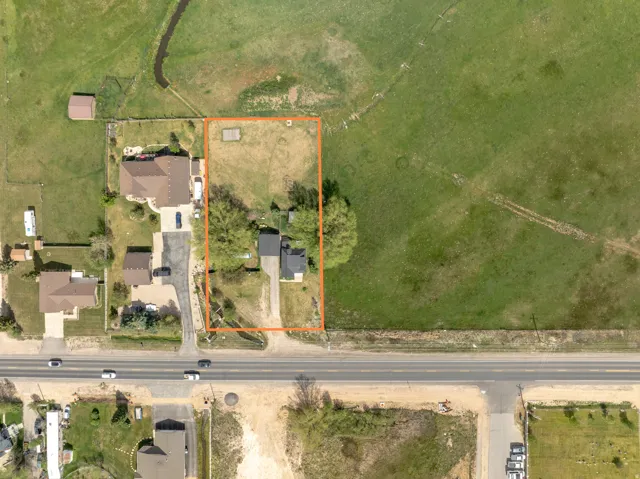 Aerial view of a residential property featuring a single-story home with a dark roof and a gravel driveway