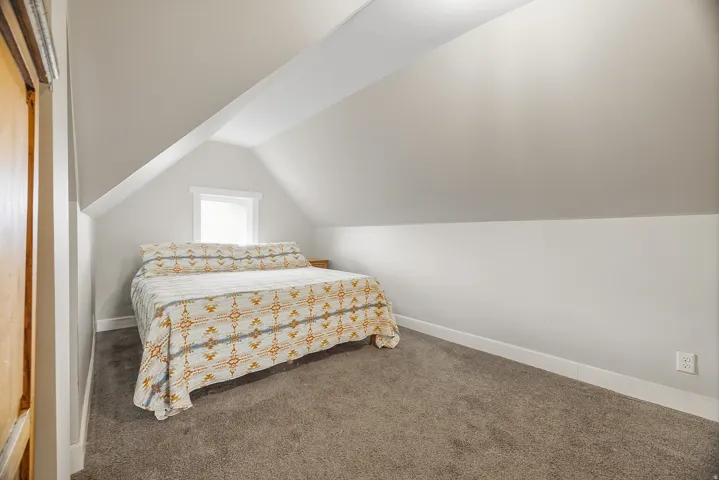 Sloped ceiling room featuring carpet flooring, neutral paint, a single window, and a wood-finish door frame