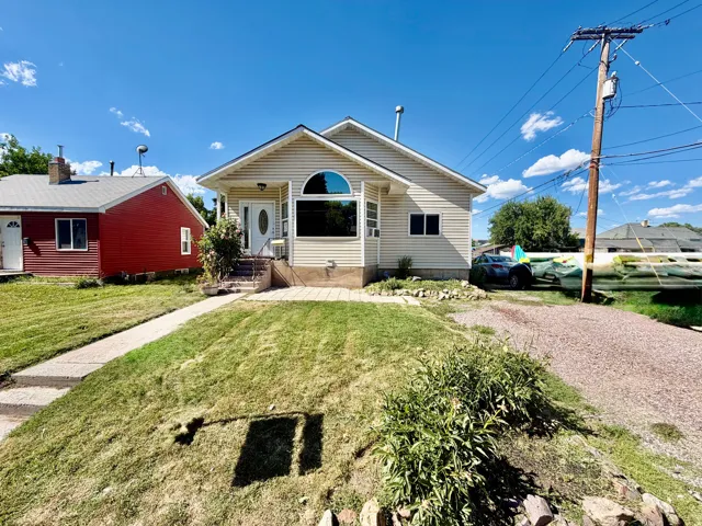 Exterior featuring light-colored siding, an arched window, a front porch with steps, a concrete walkway, and a gravel driveway