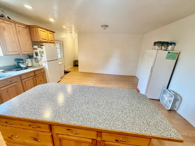 Kitchen featuring a large central island with a speckled countertop, natural wood cabinetry, recessed lighting, and wood-finish flooring