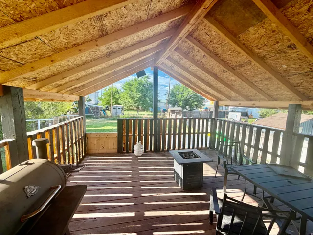 Expansive covered outdoor deck featuring a high vaulted ceiling with exposed wood beams, wood-finish flooring, and a perimeter wood railing
