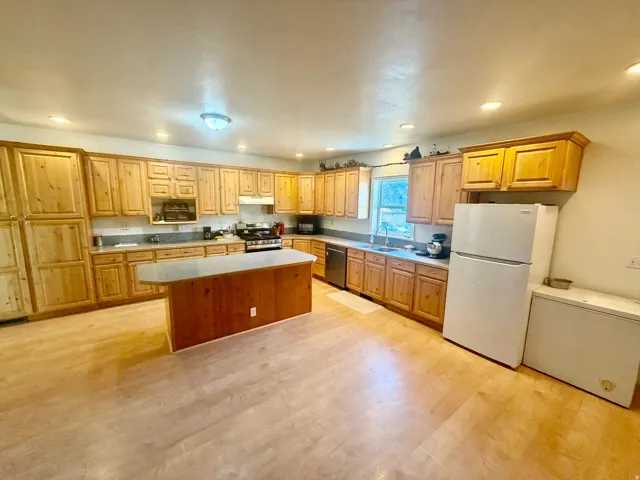 Spacious kitchen featuring light wood cabinetry, wood-finish flooring, recessed lighting, a central island with a breakfast bar, and ample counter space
