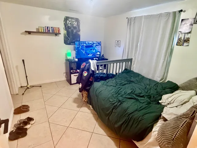 Room featuring neutral wall paint, tile flooring, a window with curtains, and a floating wall shelf