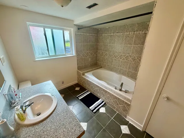 Bathroom featuring a jetted tub with tiled surround, a window, and a vanity with an integrated sink