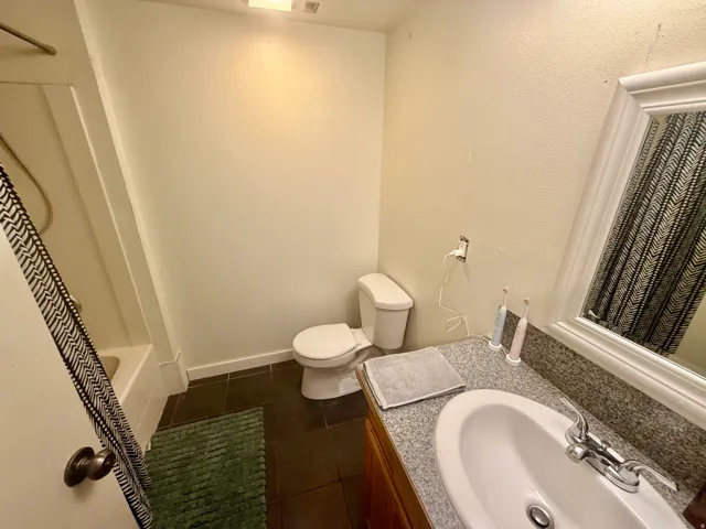 Bathroom featuring a tub/shower combination, dark tile flooring, a single vanity with an oval sink, and a framed mirror