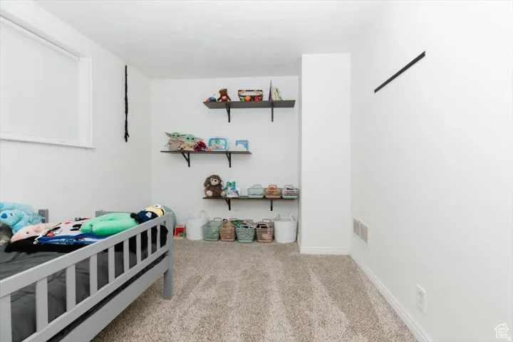 Neutral-toned room featuring a window with blinds, light-colored carpeting, white walls, and built-in shelving