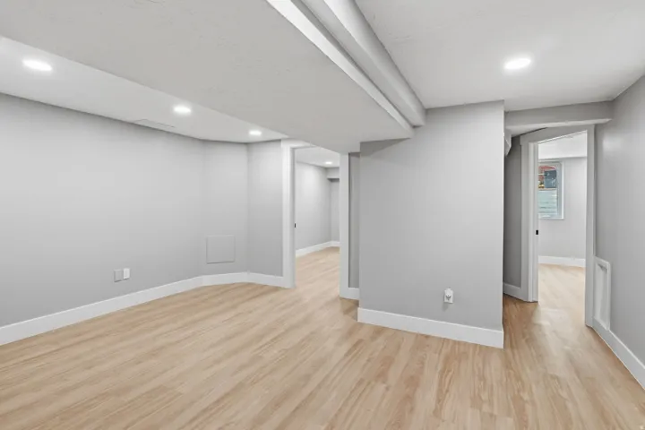 Spacious interior room featuring wood-finish flooring, recessed lighting, neutral wall tones, white baseboards, and doorways leading to additional rooms
