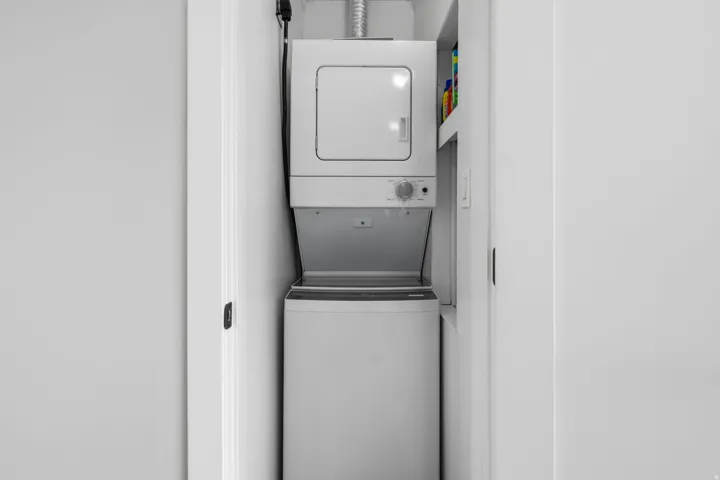 Upstairs  laundry closet featuring a stackable washer and dryer, white shelving,