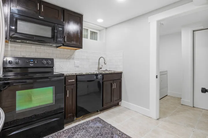 Basement Compact kitchen featuring dark wood-finish cabinetry, granite-style countertops, and subway tile backsplash