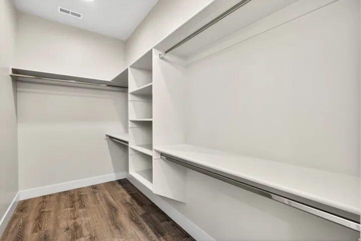 Walk-in closet featuring wood-finish flooring, built-in shelving, and multiple clothing rods