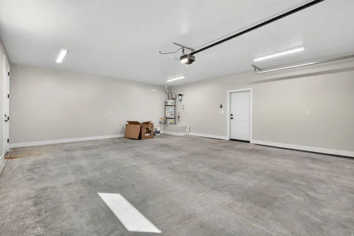Spacious garage featuring a concrete floor, two white entry doors, and overhead linear lighting fixtures