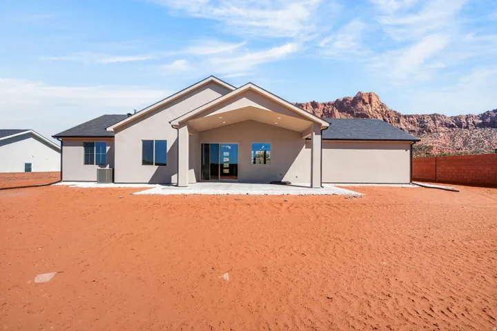 Rear exterior featuring a covered patio, sliding glass door, and a red rock mountain backdrop