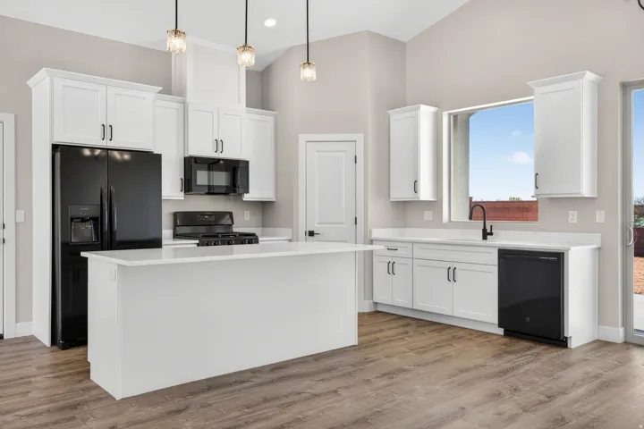 Open-concept kitchen featuring an island, white cabinetry, black appliances, wood-finish flooring, and vaulted ceilings with pendant lighting