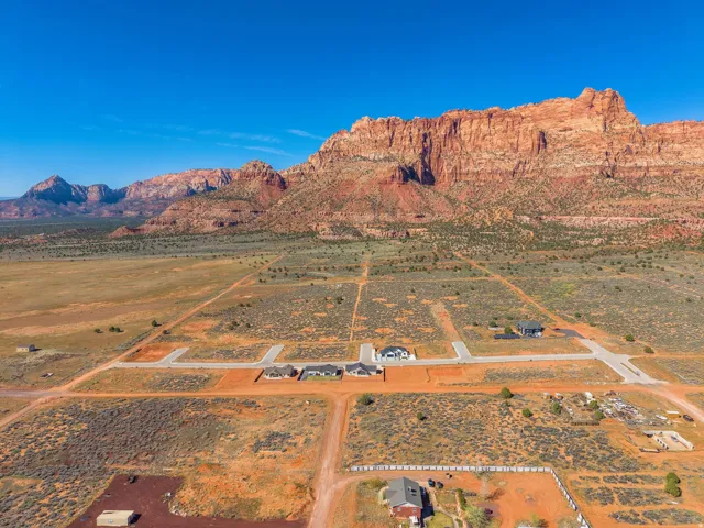 Expansive desert landscape featuring red rock mountain formations and a developing residential area with paved roads
