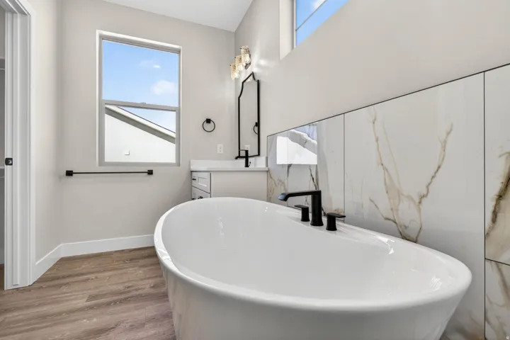 Freestanding soaking tub with matte black fixtures, set against a floor-to-ceiling accent wall featuring large format white and gold veined tiles