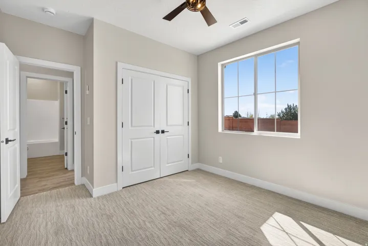 Carpeted room featuring a large window, double-door closet, ceiling fan, and painted trim