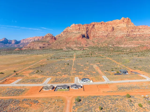 Expansive desert landscape featuring red rock mountain formations and multiple residential lots with paved road access
