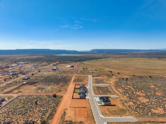 Expansive desert landscape featuring numerous undeveloped lots, a newly paved roadway, and residential structures