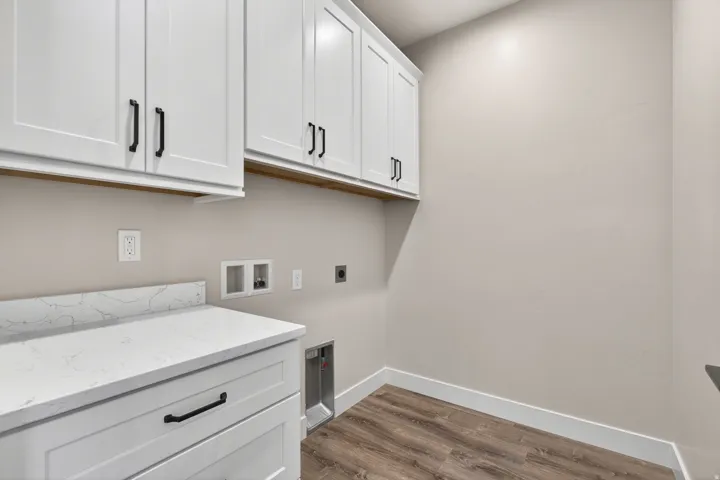Laundry area featuring white shaker-style cabinetry with matte black hardware, a light-toned countertop with veining, and wood-finish flooring
