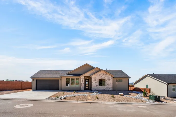 Contemporary stucco exterior with stone accents, dark asphalt shingle roof, integrated two-car garage, and desert-adapted landscaping