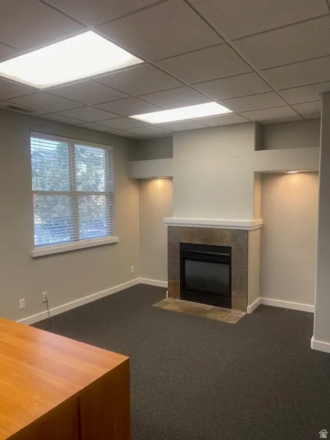 Interior space featuring a tiled fireplace with mantel, recessed wall niches with accent lighting, and a drop ceiling with integrated lighting panels
